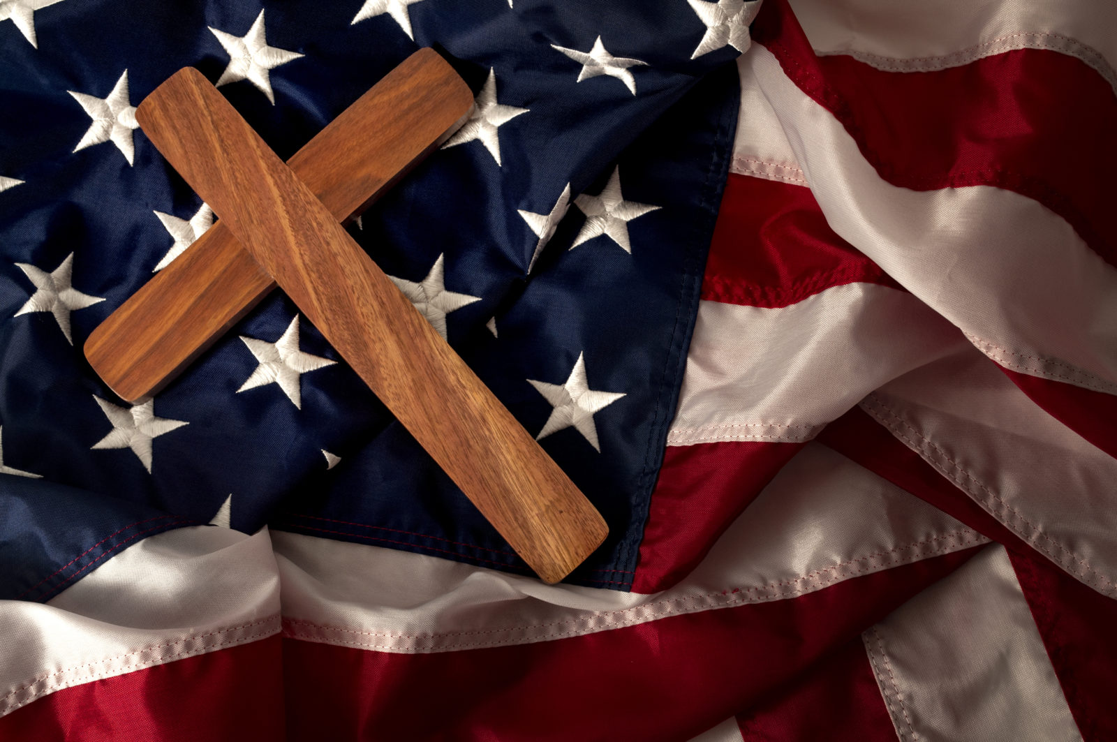 Evangelical America, christianity, born again christian and fundamentalist religious right concept with close up on a wooden cross or crucifix on the american flag with dramatic light and moody tone