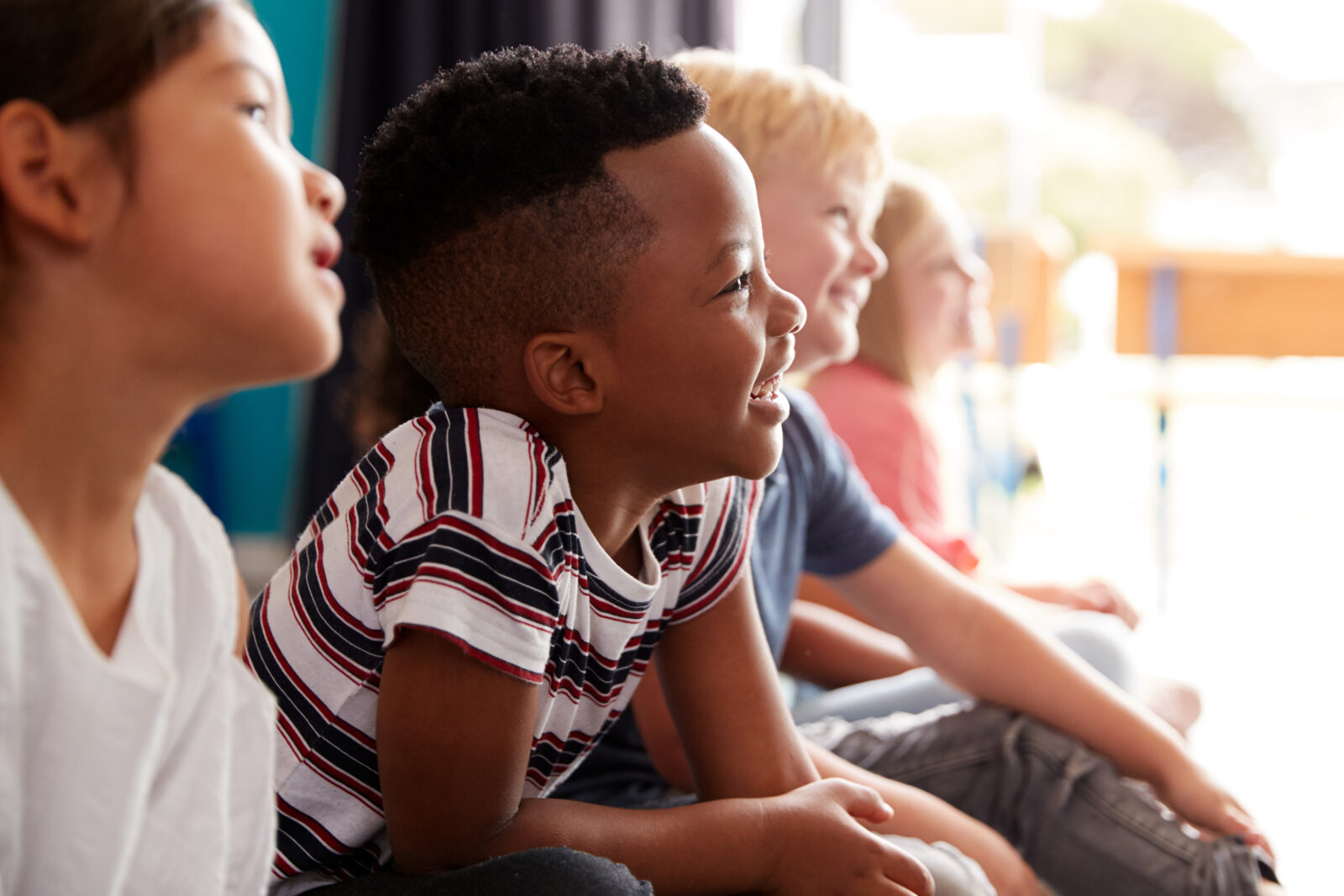 Group Of Elementary School Pupils Sitting On Floor Listening To Teacher