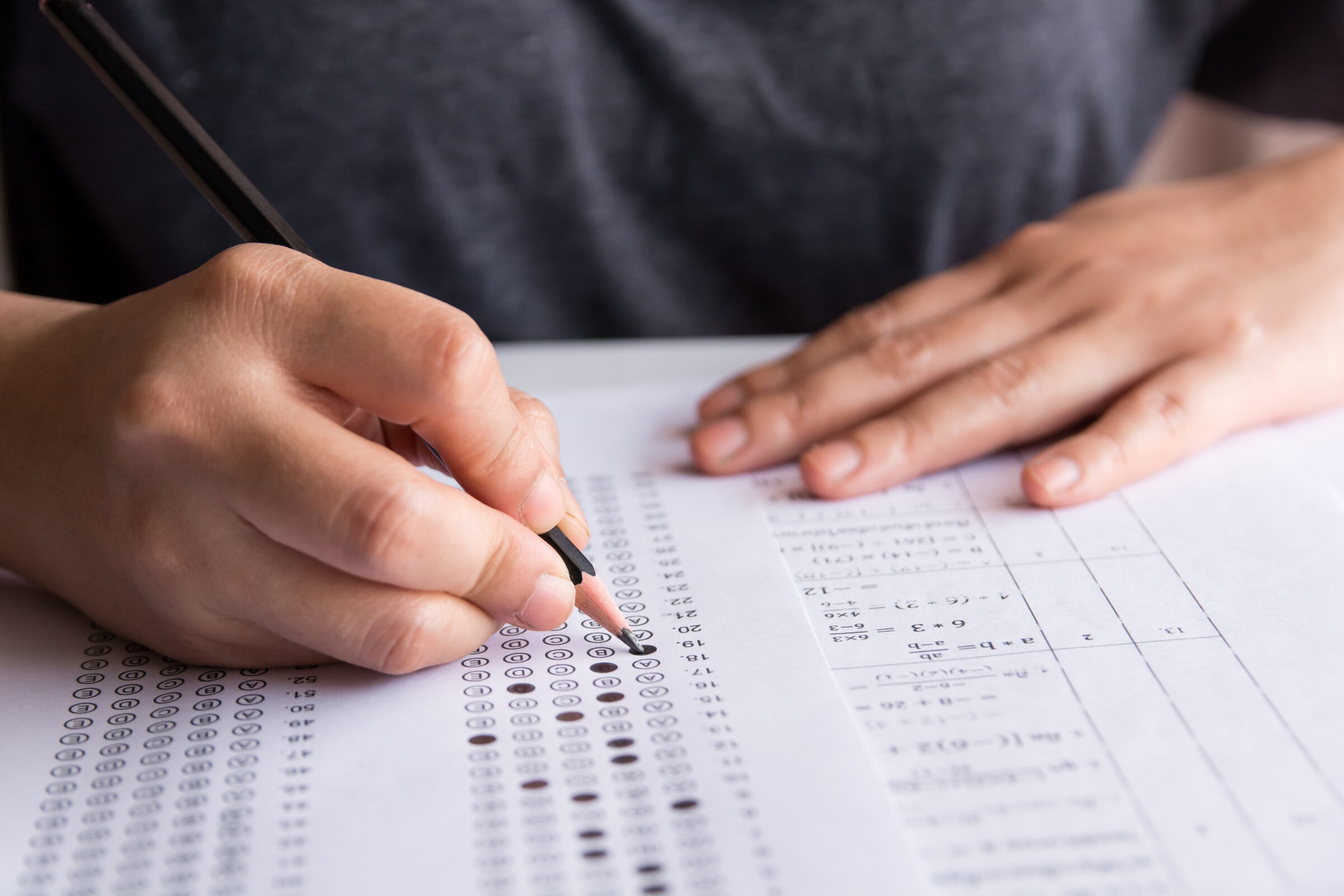 Exam. Students holding pencil writing selected choice on answer sheets and Mathematics question sheets. students testing doing examination. school exam